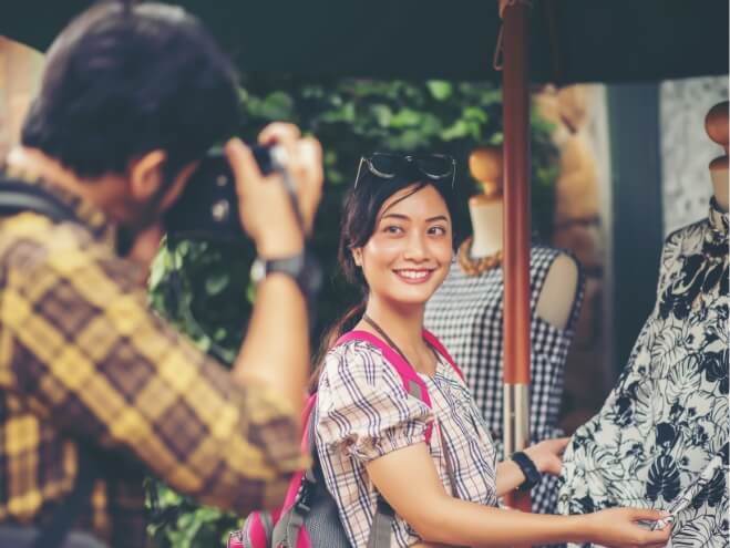 Behind-the-scenes of a video shoot, with a female talent smiling at the camera while the crew films under an umbrella.
