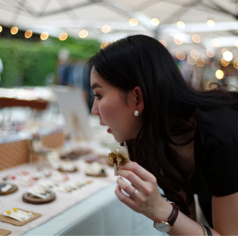 Woman browsing handmade jewellery at an outdoor market stall, closely examining a ring with curiosity.