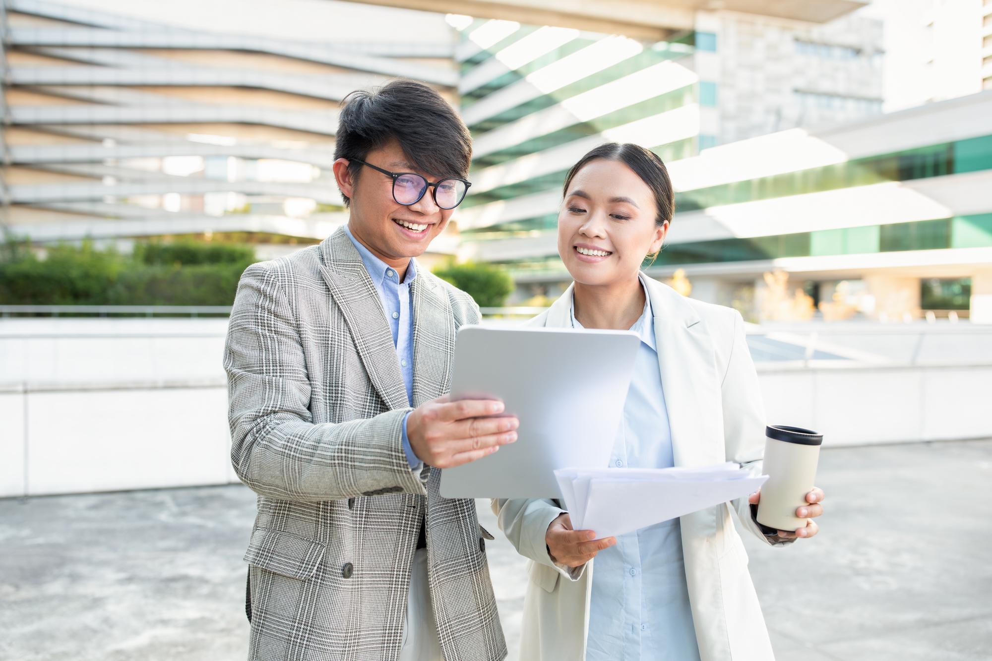 Young professionals smiling while reviewing documents outdoors